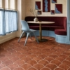 Elegante recanto para refeições com piso de ladrilhos de terracota em formato de escamas de peixe, banqueta bordô, cadeira azul-clara e arte geométrica na parede.