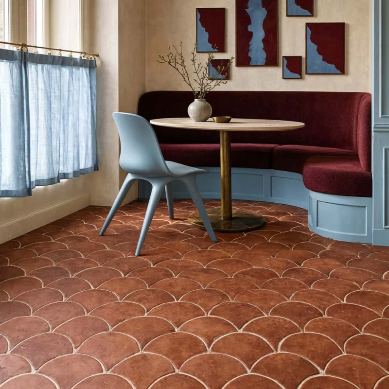 Elegante recanto para refeições com piso de ladrilhos de terracota em formato de escamas de peixe, banqueta bordô, cadeira azul-clara e arte geométrica na parede.