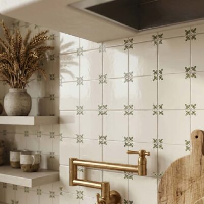 A kitchen backsplash featuring ceramic wall tiles with green hand painted leaf motifs